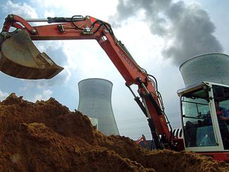 In front of the cooling towers of the Gundremmingen nuclear power plant, earth is being excavated with an excavator.