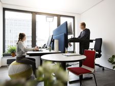 In an office, a woman and a man work at height-adjustable desks.