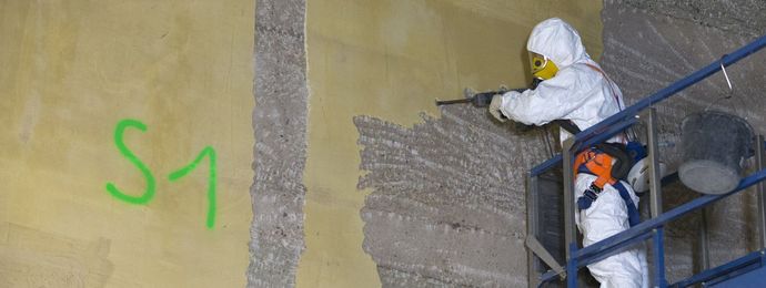 A man dressed in a protective suit removes the surface of the wall